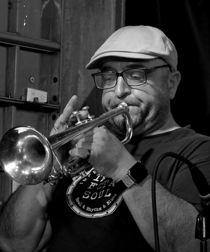Luis Mur tocando la trompeta en un concierto, con gorra y gafas.